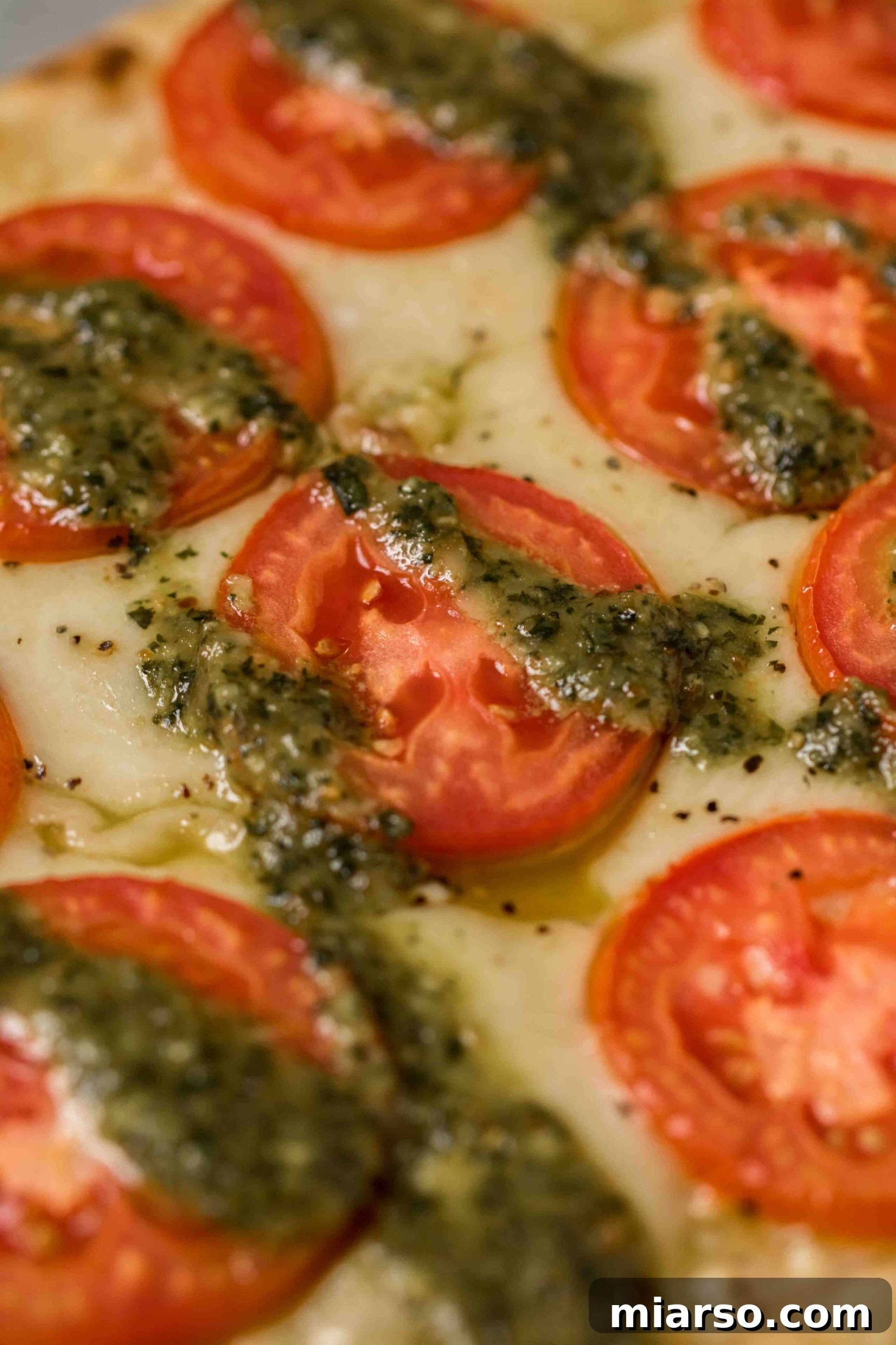 Close-up of melted mozzarella, fresh tomato slices, and vibrant pesto on a flatbread pizza
