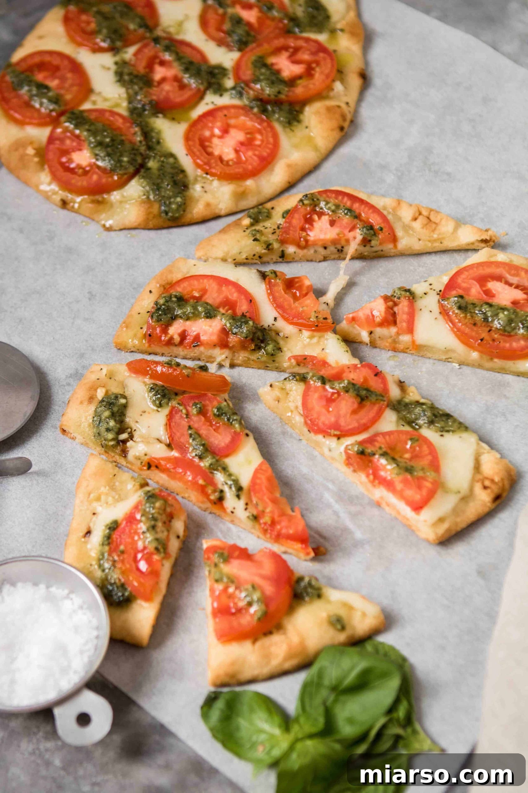 Perfectly sliced flatbread pizzas garnished with sea salt and fresh basil leaves on the side.