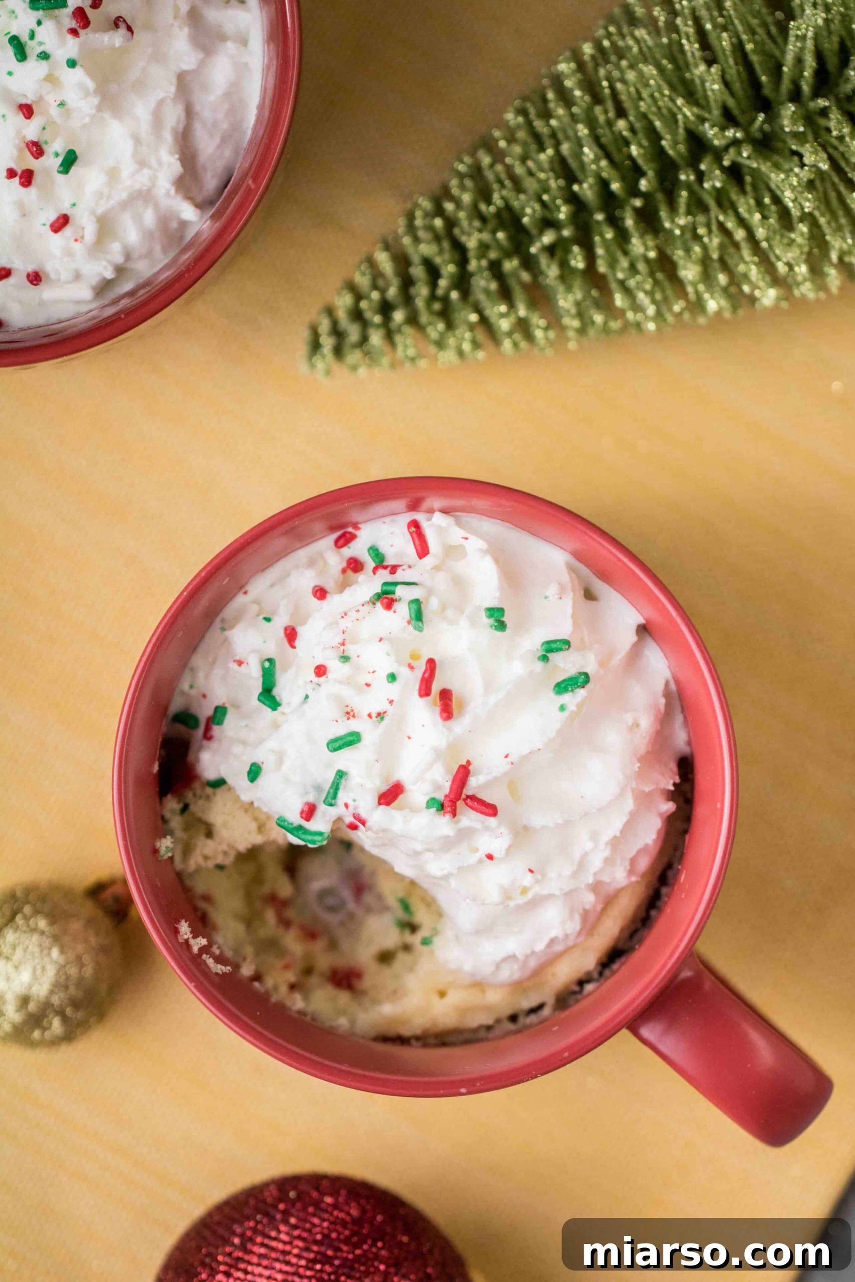 Christmas mug cake topped with whipped cream and sprinkles, ready to be eaten.