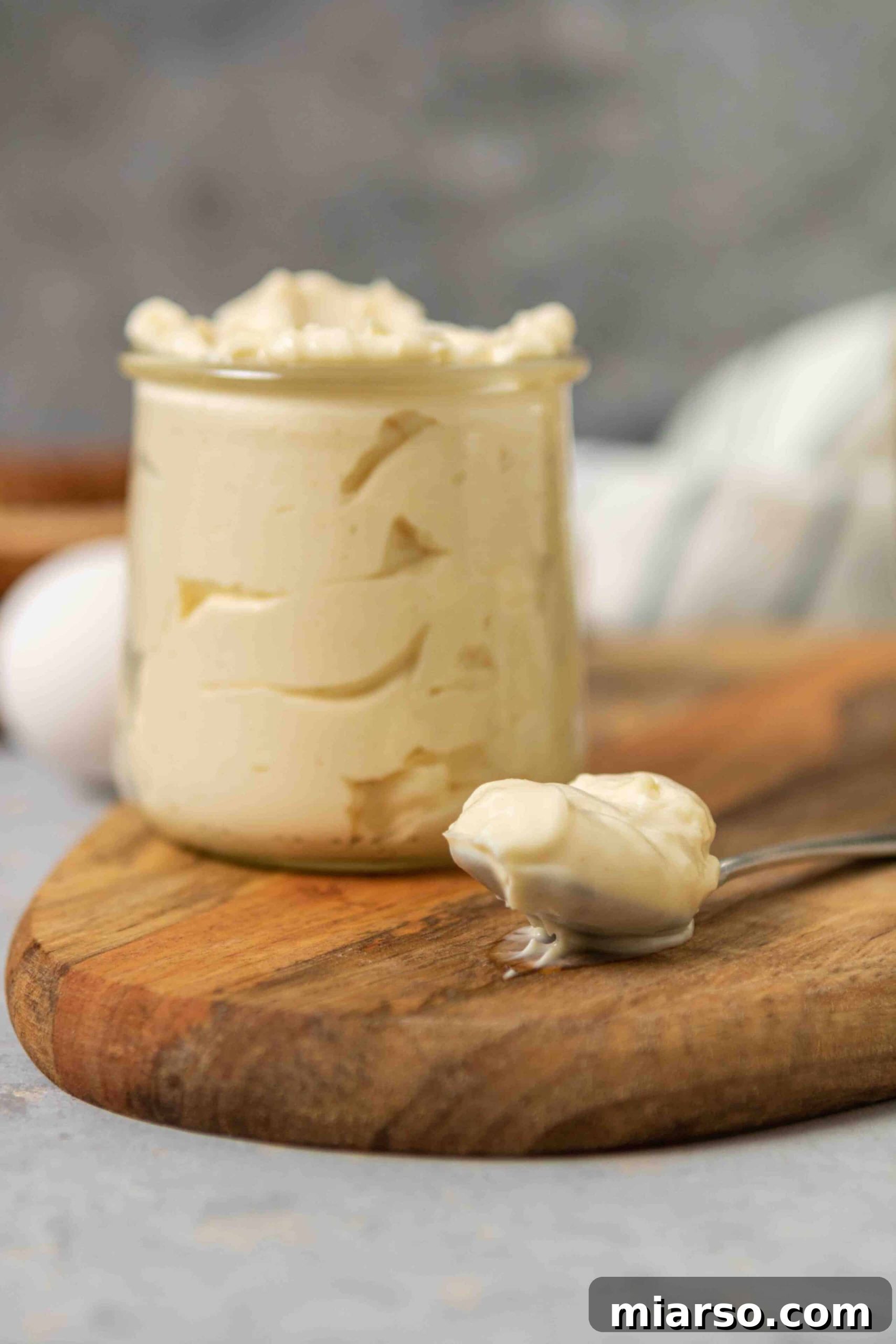 A jar of homemade mayonnaise with a spoon resting beside it, highlighting its rich texture.