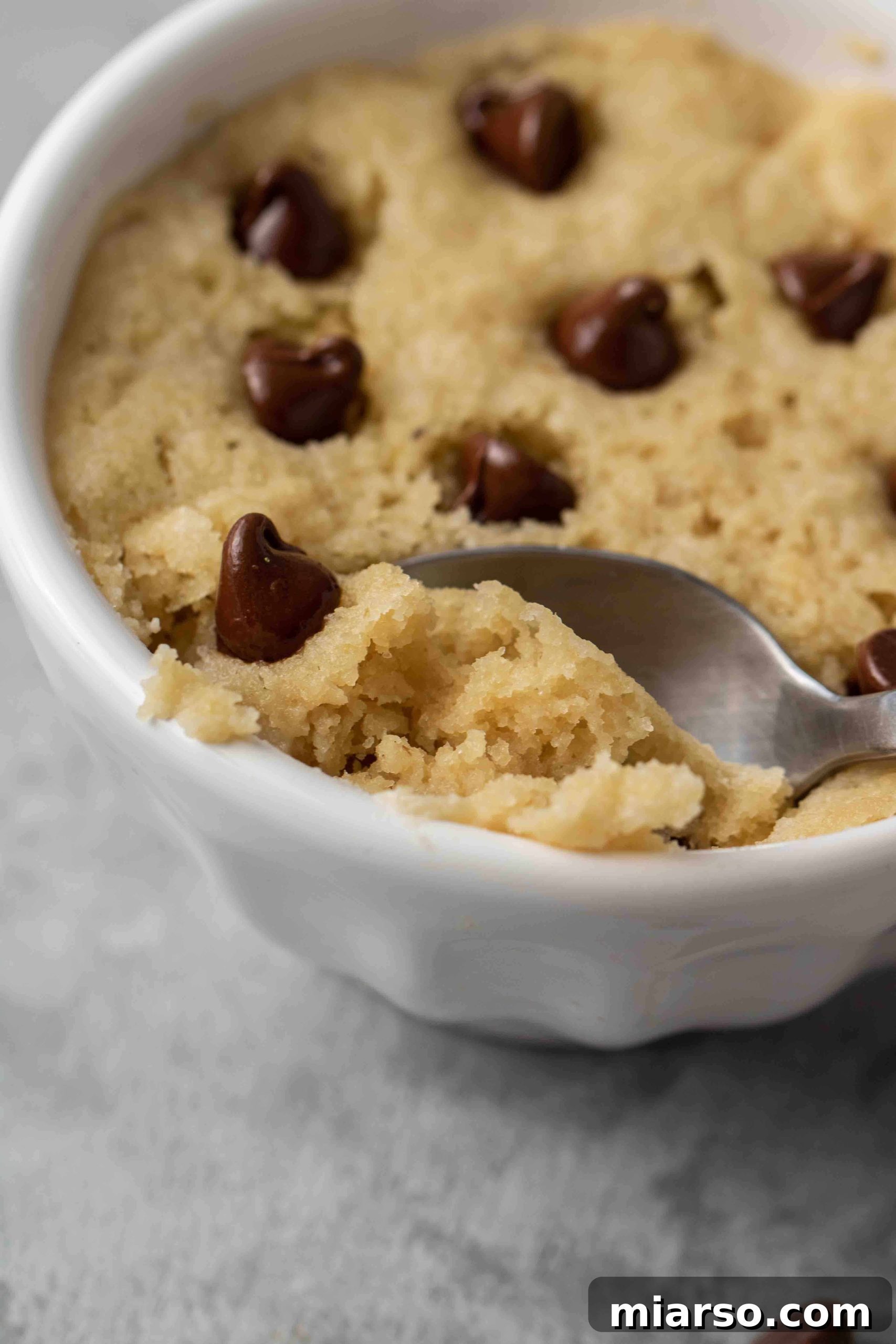Close-up of a freshly baked healthy vegan chocolate chip mug cookie, showcasing its golden-brown edges and melted chocolate chips.