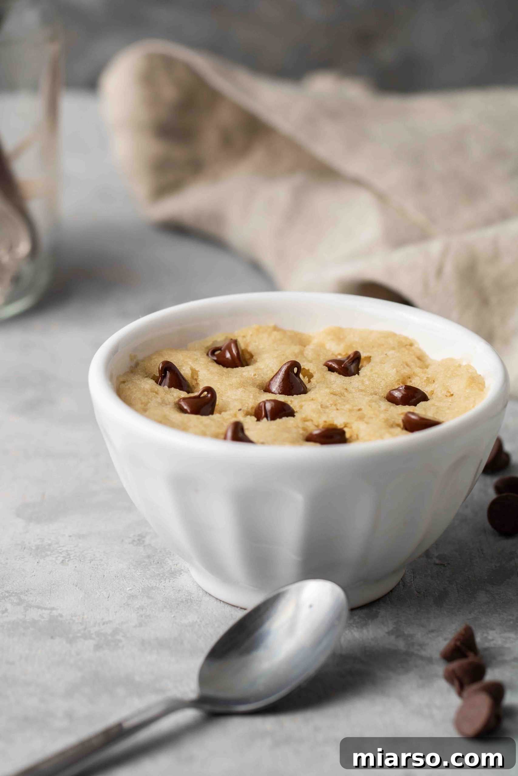 A spoon resting next to a healthy vegan chocolate chip mug cookie, highlighting its rich texture and melty chocolate.