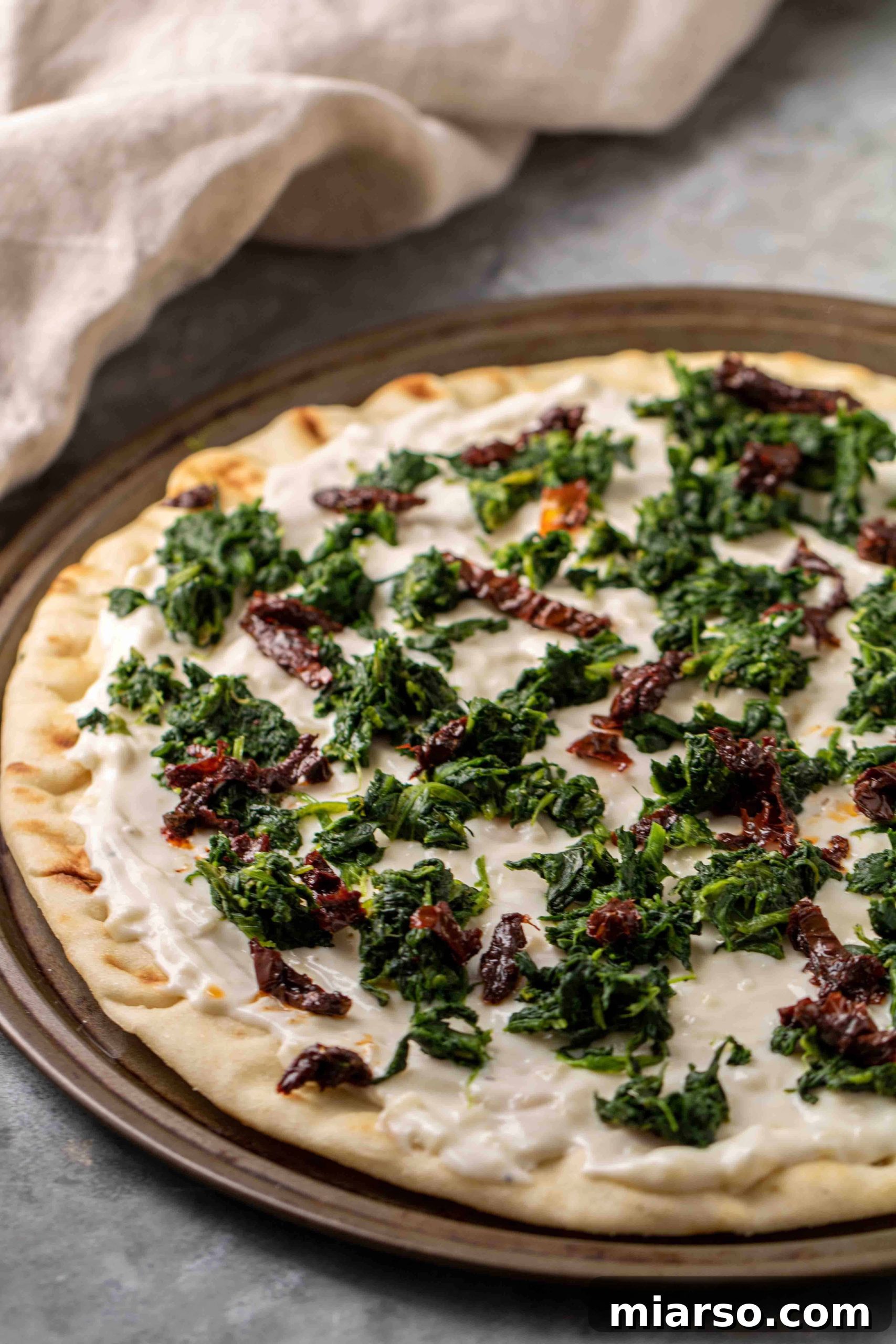 Spinach pizza with white sauce before baking, showcasing fresh ingredients