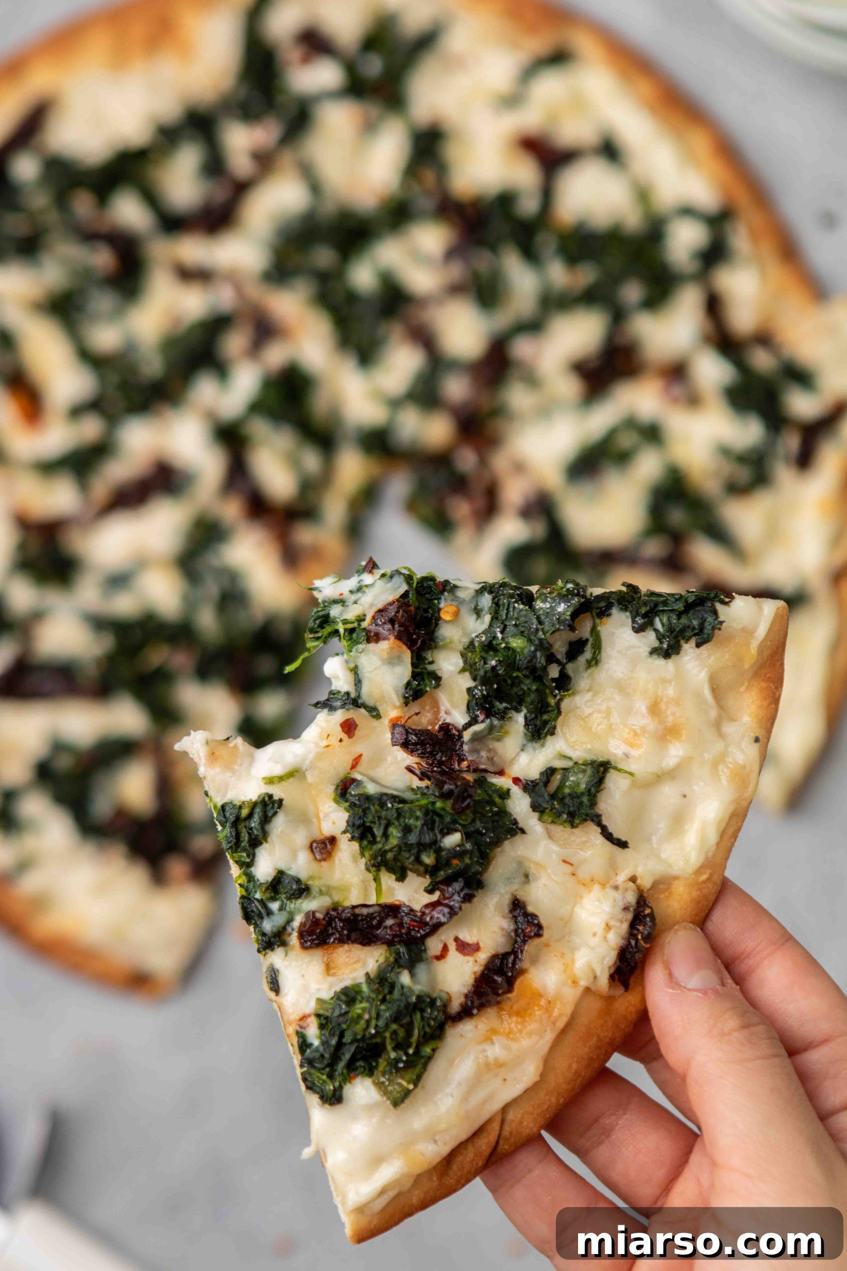 Close up of a perfect slice of spinach pizza with white sauce