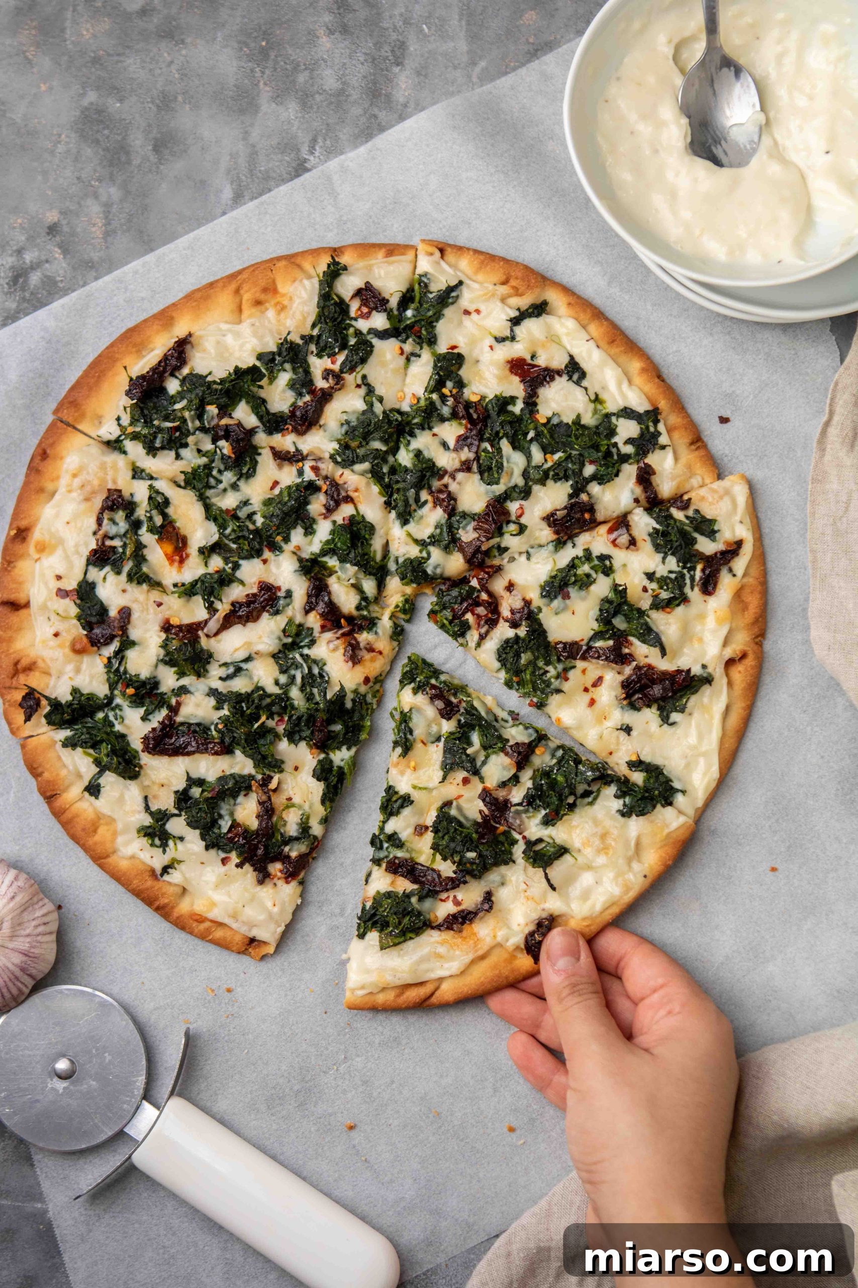 Hand grabbing a slice of hot white spinach pizza