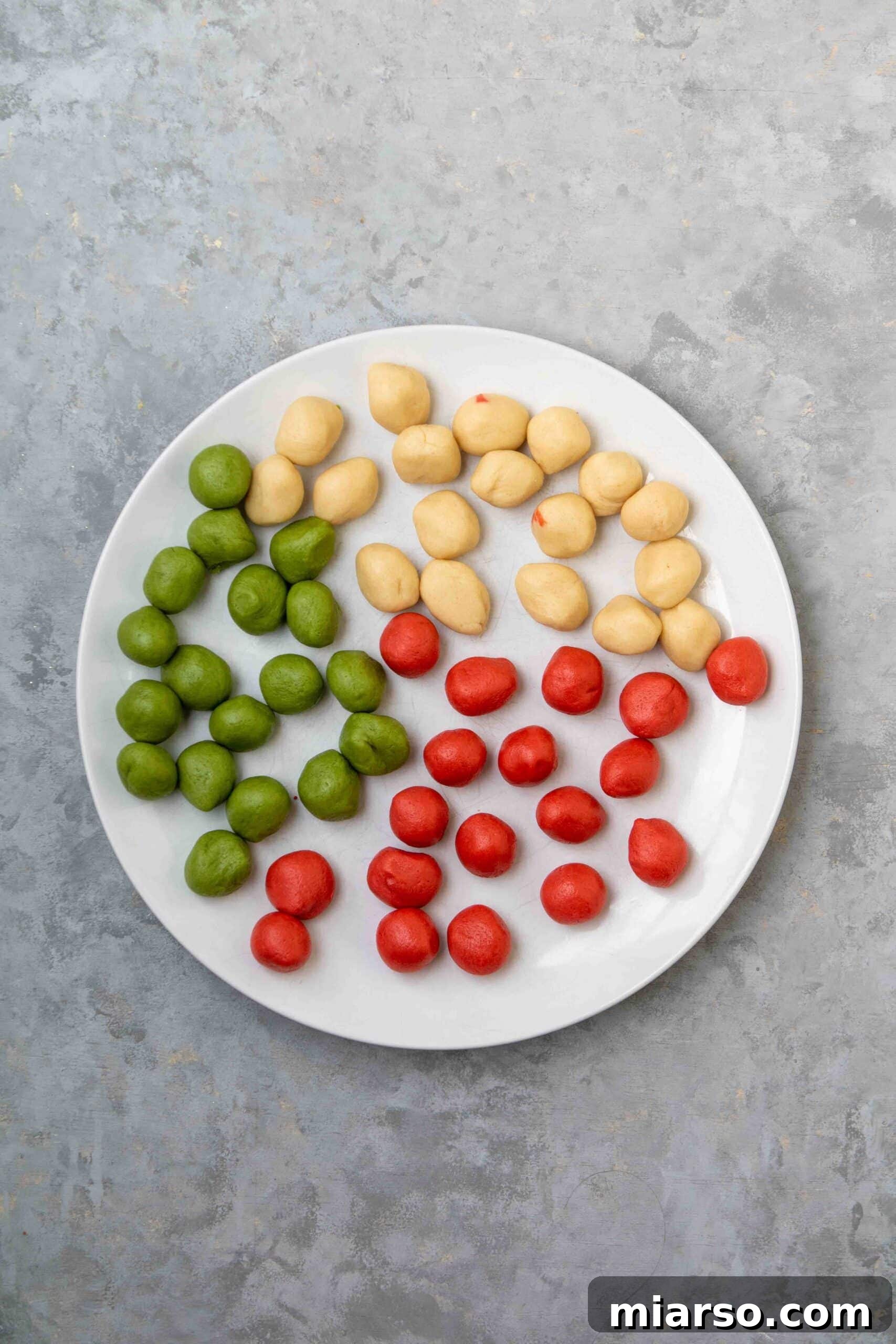Scoops of red, green, and white cookie dough on a plate, ready to be marbled