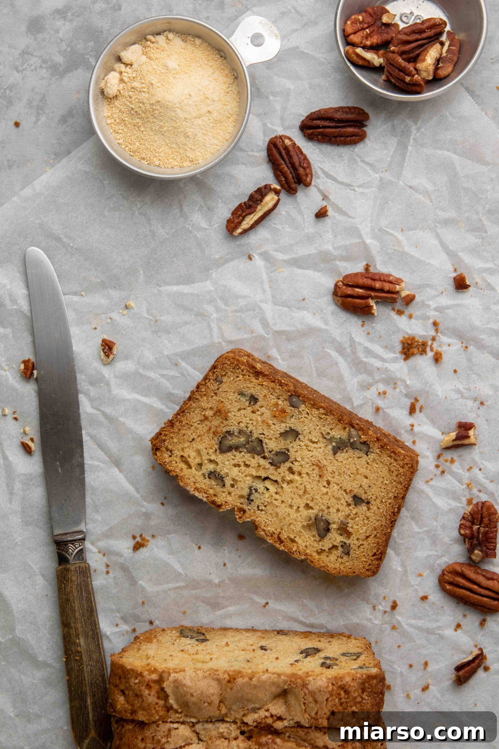 One perfect slice of maple pecan cake next to scattered pecan pieces, ready to be devoured.