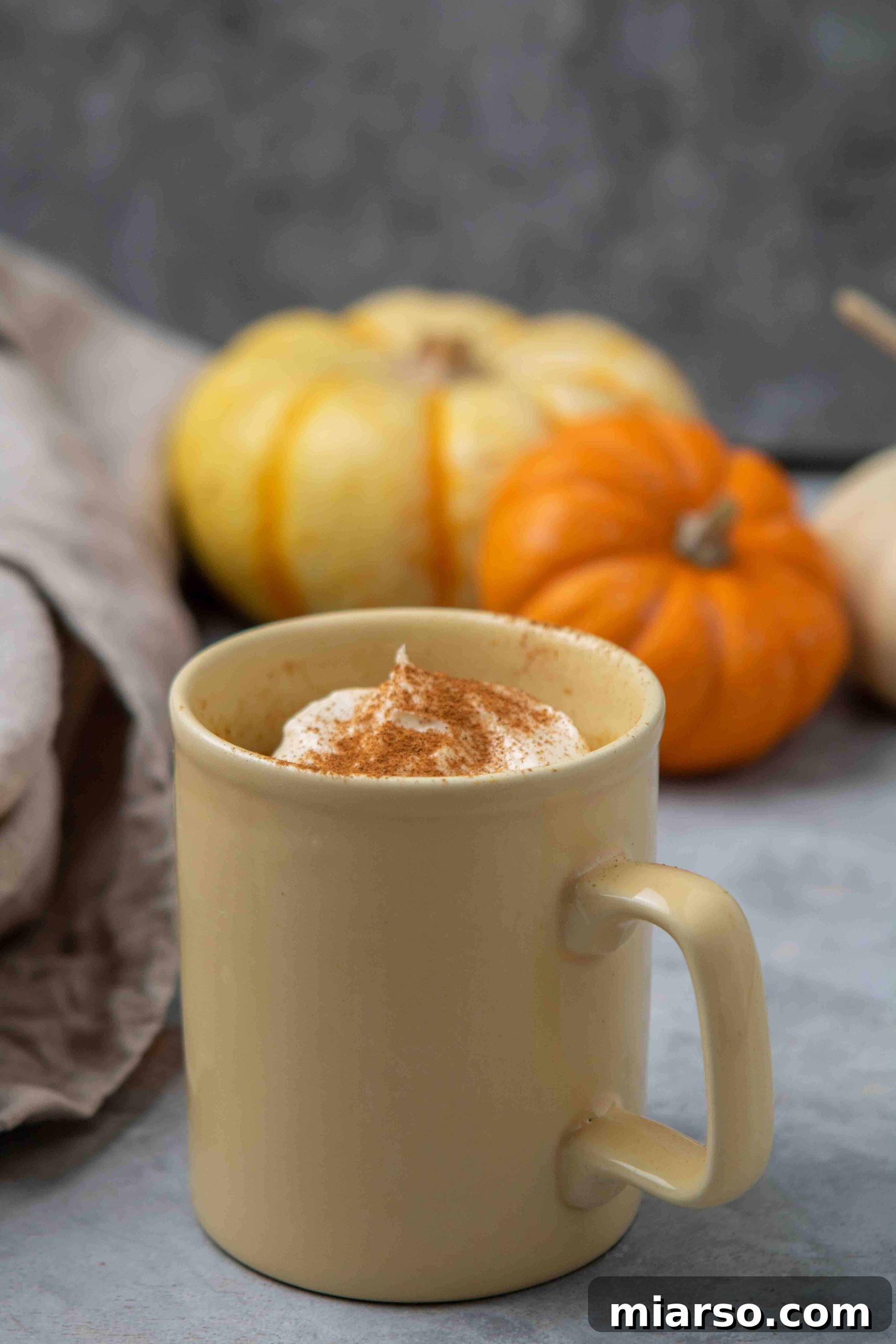 A delicious pumpkin cake in a vibrant yellow mug, topped with a dollop of white frosting and a sprinkle of cinnamon, perfect for fall.