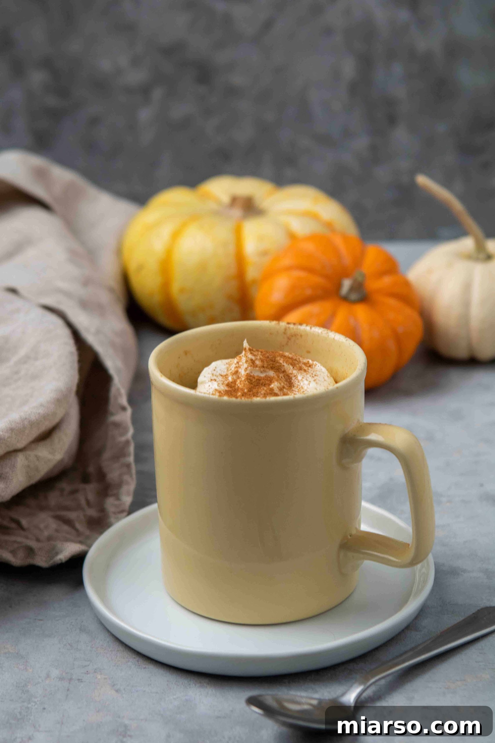 Close up shot of a fluffy, moist pumpkin cake in a yellow mug with a spoon, showing its appealing texture.
