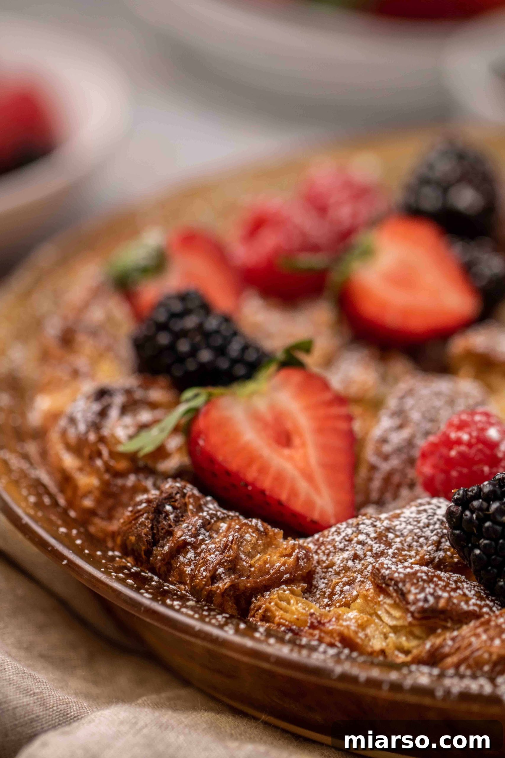 Heavenly Croissant French Toast Bake 2 Golden Croissant French toast bake generously topped with fresh berries and a dusting of powdered sugar, served in a rustic pie dish.