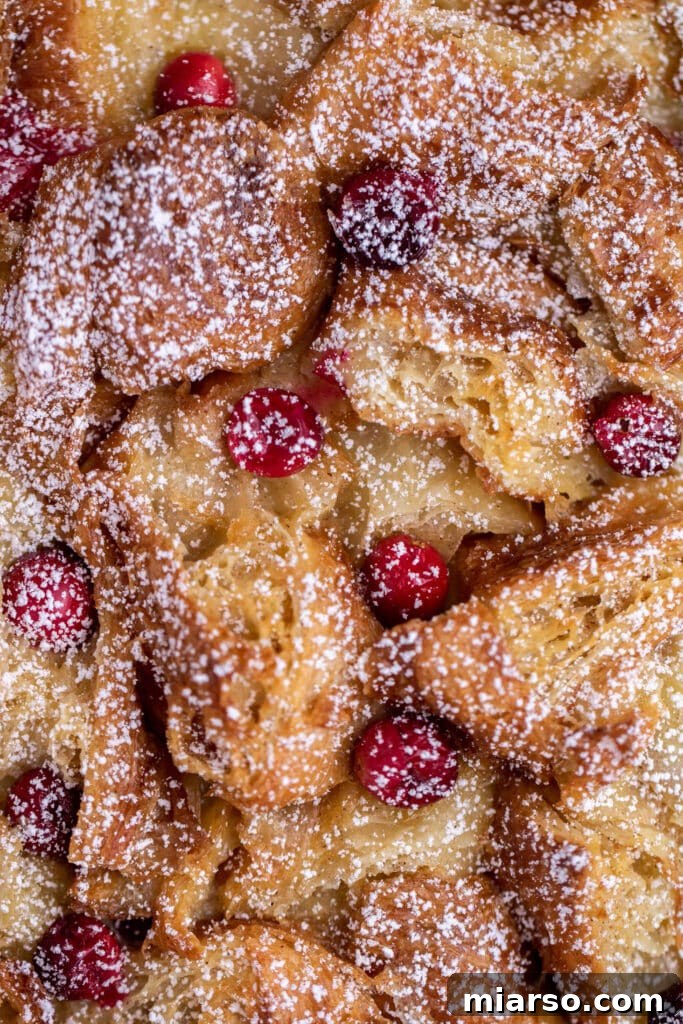 Heavenly Croissant French Toast Bake 13 Overhead shot of a Croissant French toast bake in a pie dish, topped with a generous amount of fresh berries and powdered sugar, ready to be served.