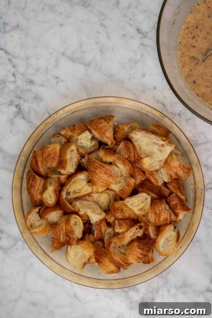 Heavenly Croissant French Toast Bake 8 Torn croissant pieces being gently folded into the egg custard in a mixing bowl.