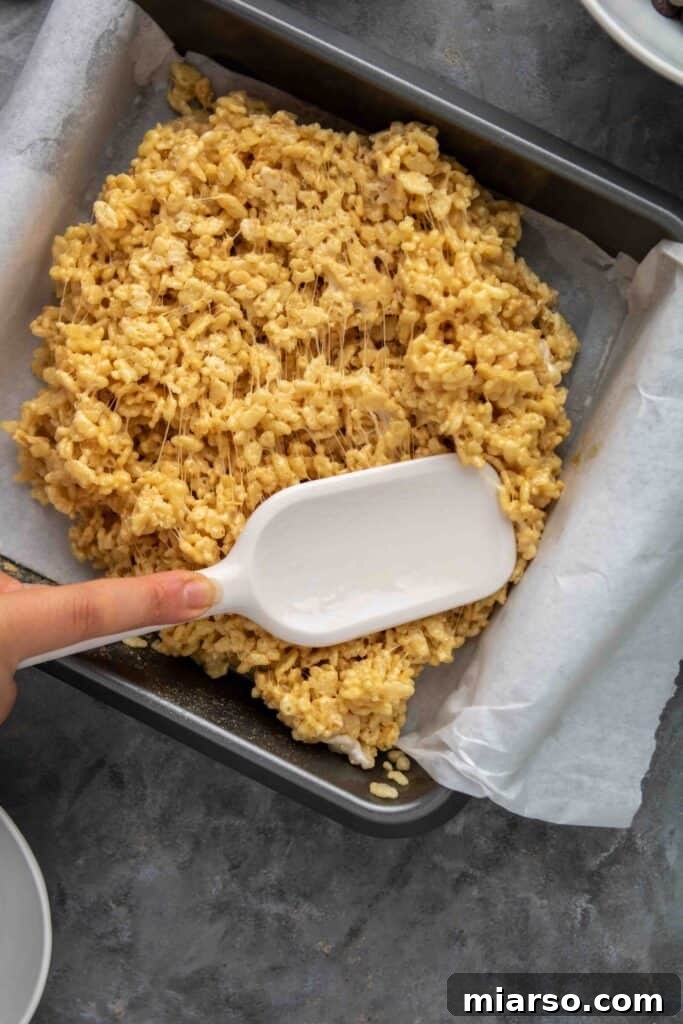 No-Bake Chocolate Peanut Butter Crispy Bars 9 Hand pressing peanut butter rice krispie treats into a pan