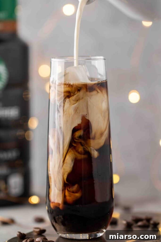 Starbucks Velvety Vanilla Cold Brew 13 Pouring vanilla sweet cream over a glass of cold brew coffee and ice, creating beautiful swirls.