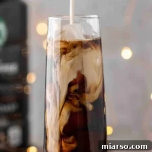 Pouring vanilla sweet cream over a glass of cold brew coffee and ice, showing the finished drink.