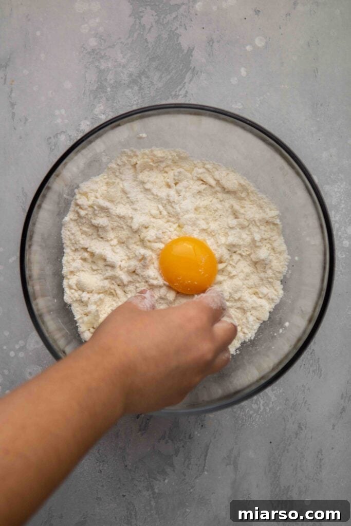 Image showing butter being gently worked into the flour mixture with fingertips.