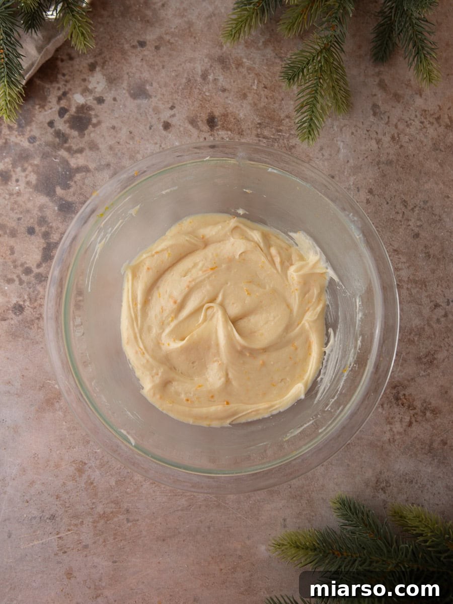 Creamy orange-speckled frosting in a glass bowl on a stone countertop.