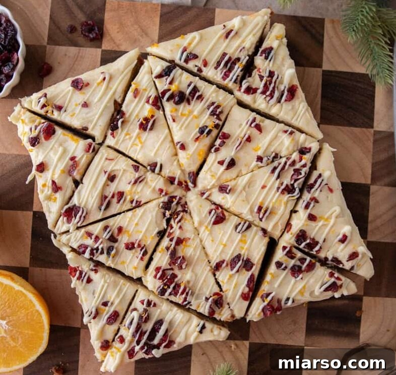 Overhead view of frosted cranberry bliss bars cut into triangles and arranged neatly on a wooden board.
