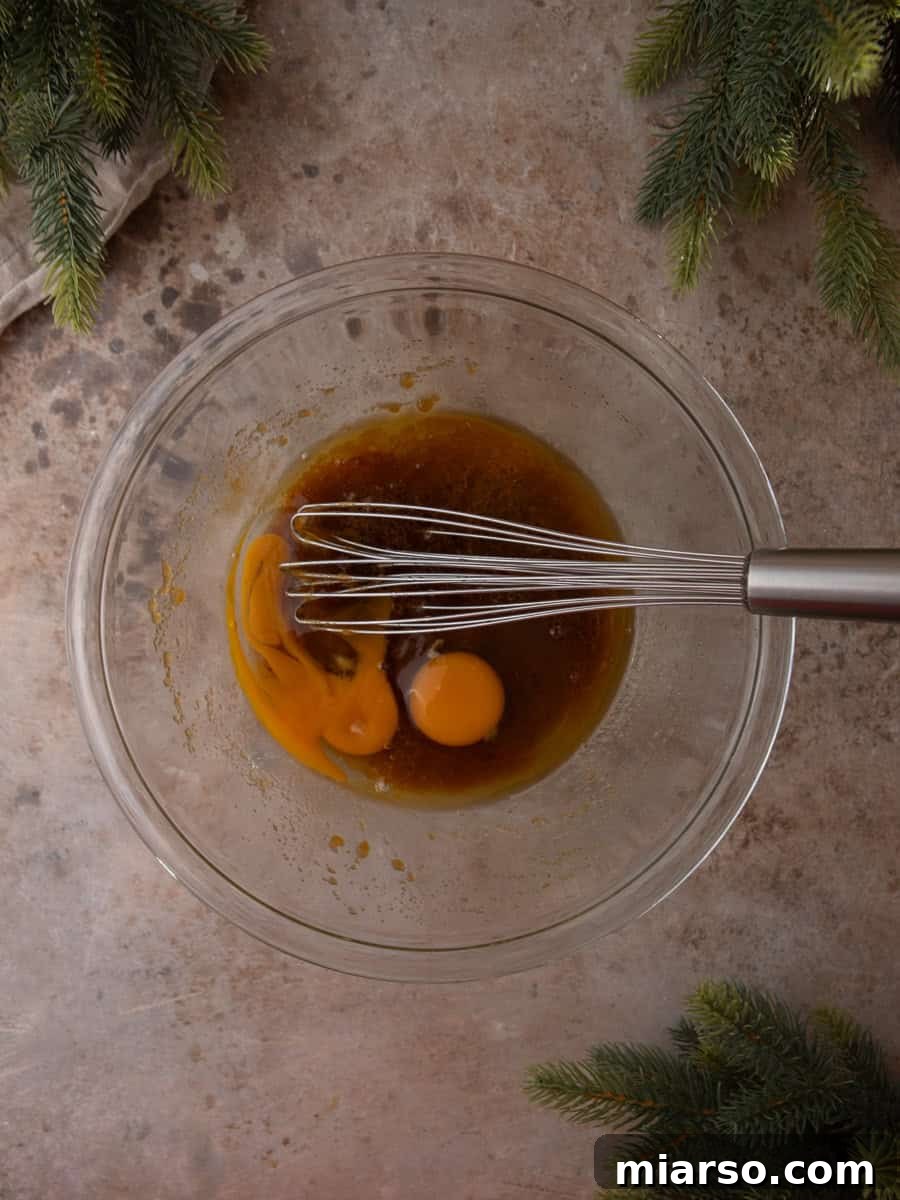 Eggs added to the melted butter and brown sugar mixture in a glass bowl with a whisk.
