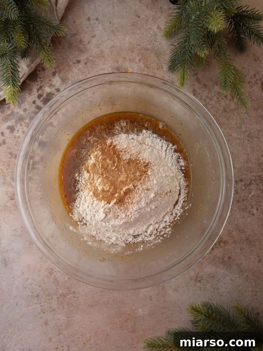 Flour and warm spices sitting on top of wet batter in a glass mixing bowl before folding.