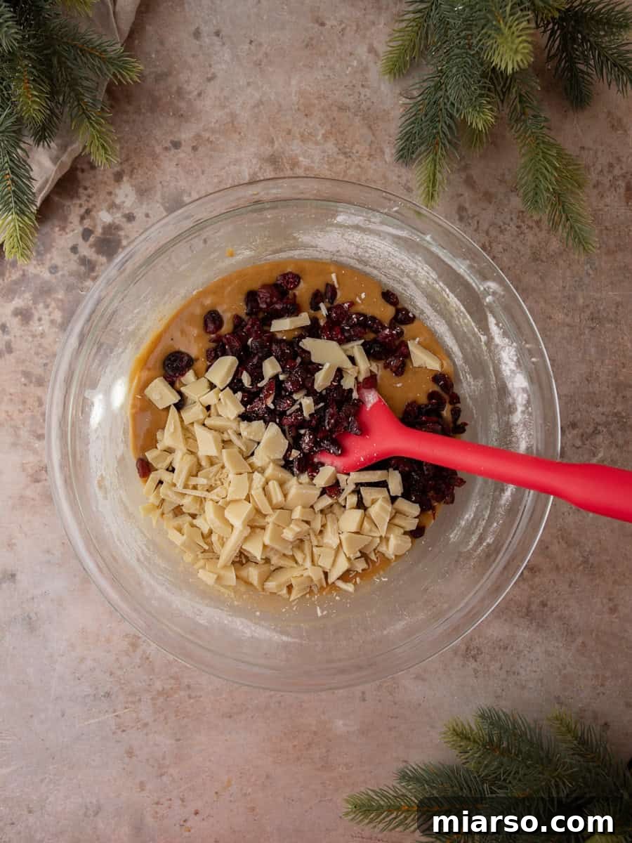Blondie batter mixed with dried cranberries and chopped white chocolate in a glass bowl.
