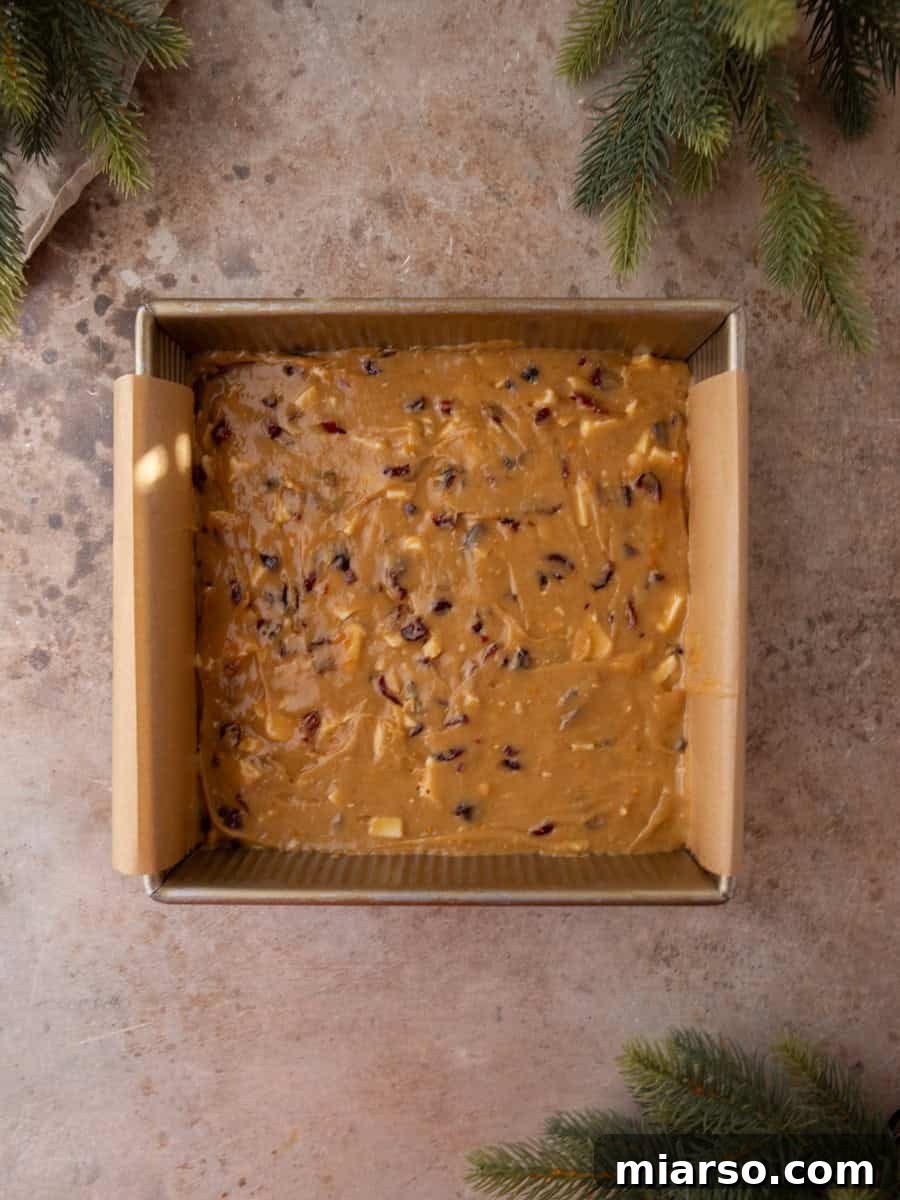 Cranberry blondie batter spread evenly in a parchment-lined square baking pan.
