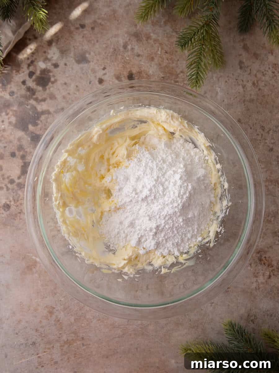 Cream cheese and powdered sugar being mixed in a glass bowl to make frosting.
