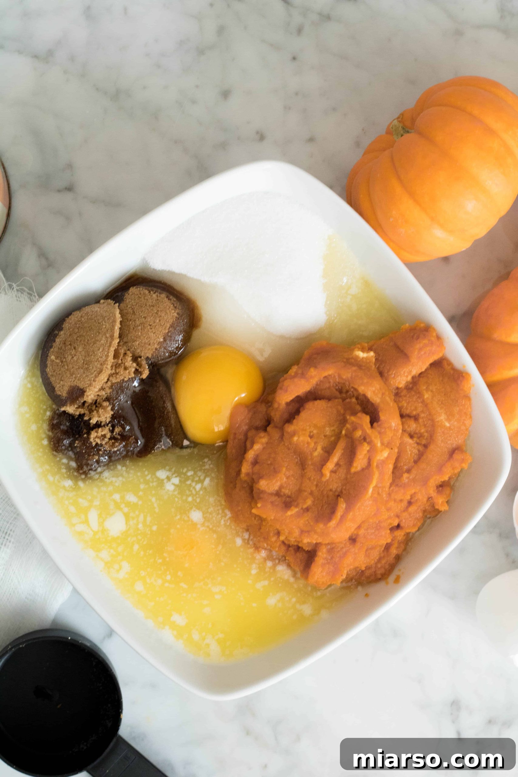 A visually appealing flat lay of the wet ingredients for pumpkin chocolate chip muffins – including vibrant pumpkin puree, golden brown sugar, white granulated sugar, eggs, and melted butter – perfectly arranged before mixing.