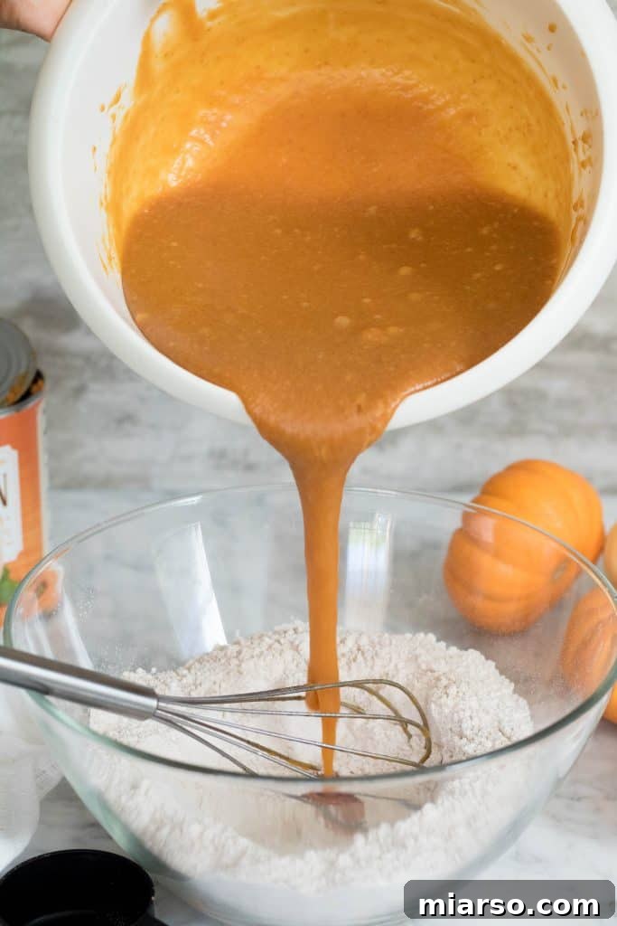 The vibrant orange wet ingredients for the pumpkin muffins being carefully poured into the center of the bowl containing the dry ingredients, ready for gentle mixing.