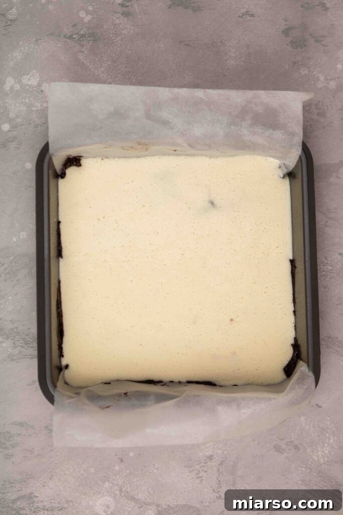 Pouring cream cheese layer onto the brownie base