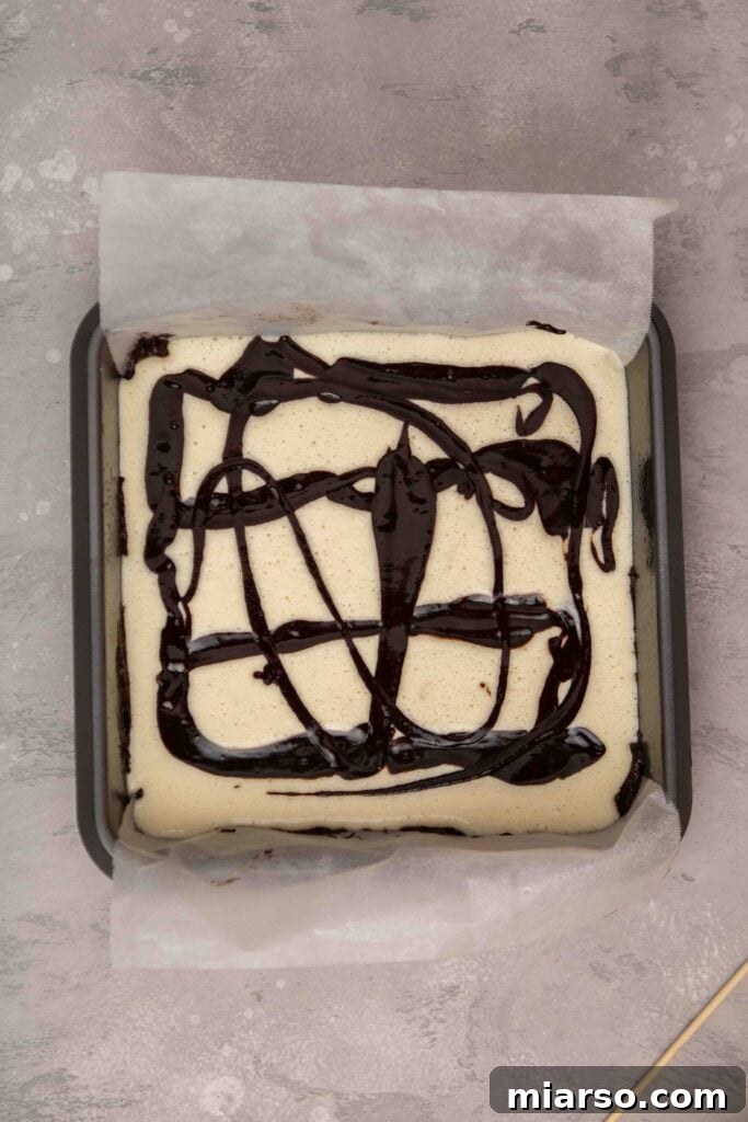 Adding thinned out brownie batter over the cream cheese layer for swirling
