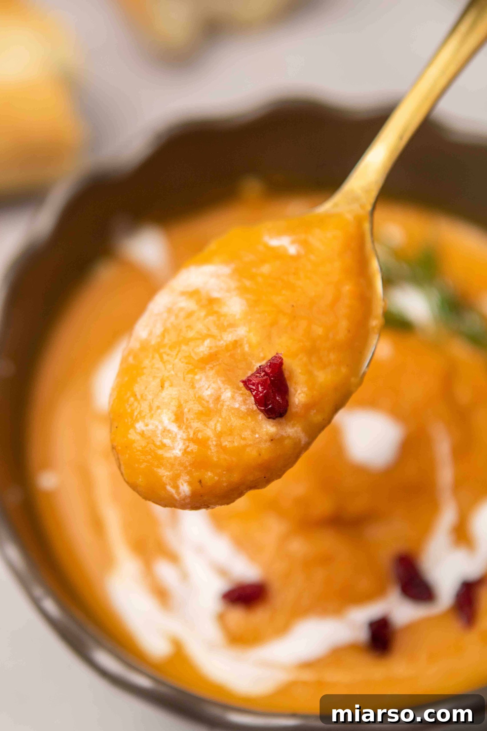 Spoonful of sweet potato carrot soup, showcasing its rich, vibrant color and creamy texture.