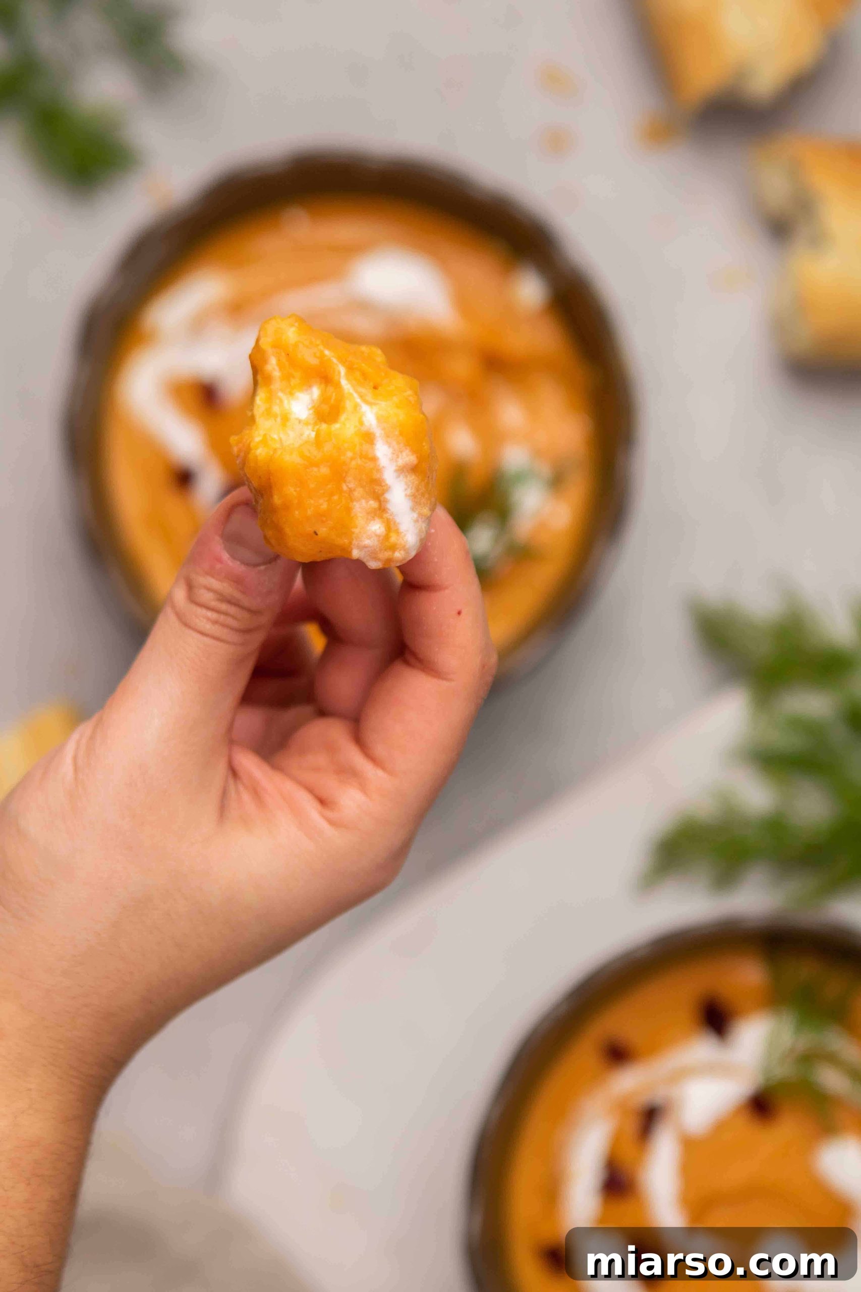 A slice of crusty bread dipped into a bowl of rich carrot and sweet potato soup.