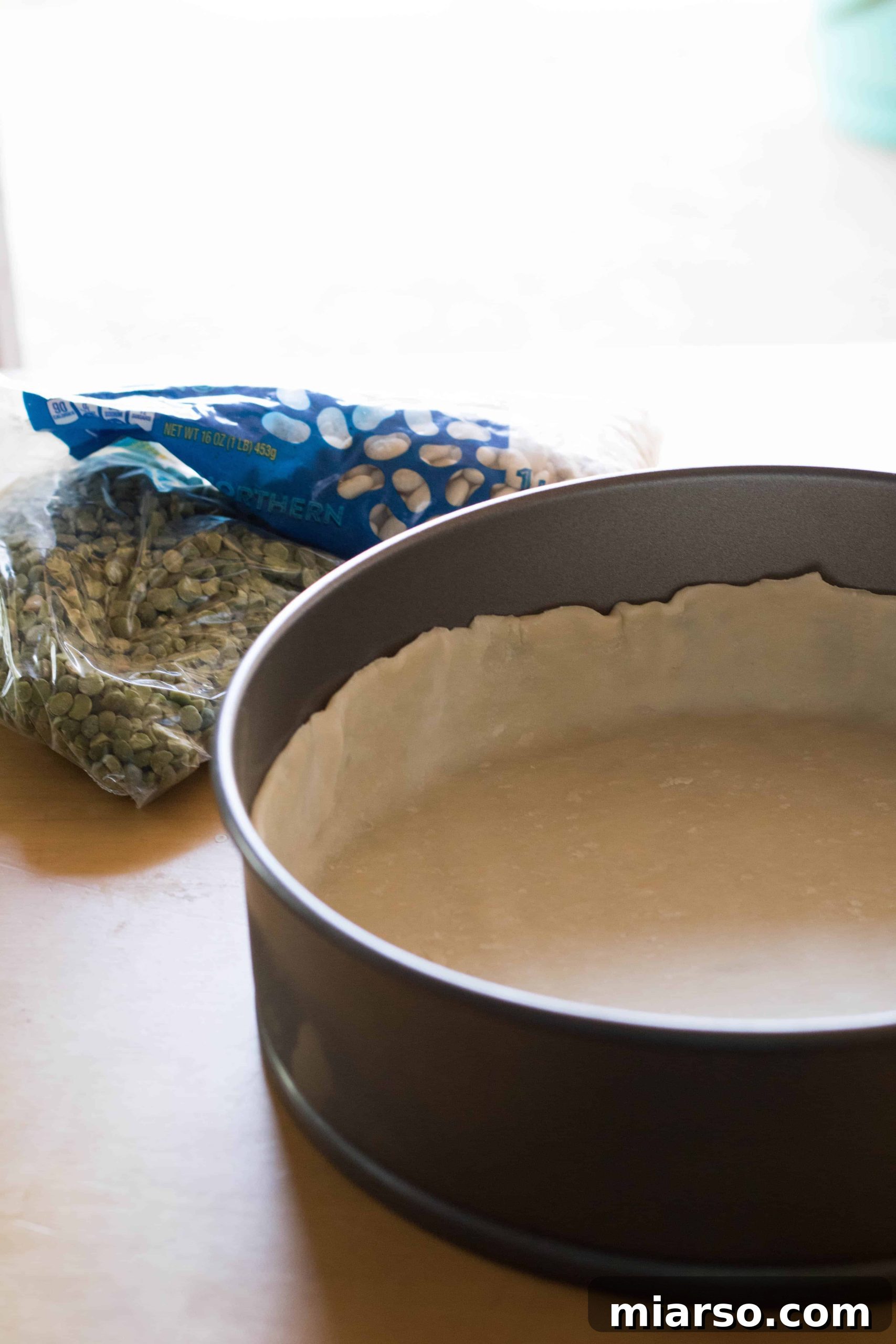 Chilled pie crust being prepared for blind baking with plastic wrap.