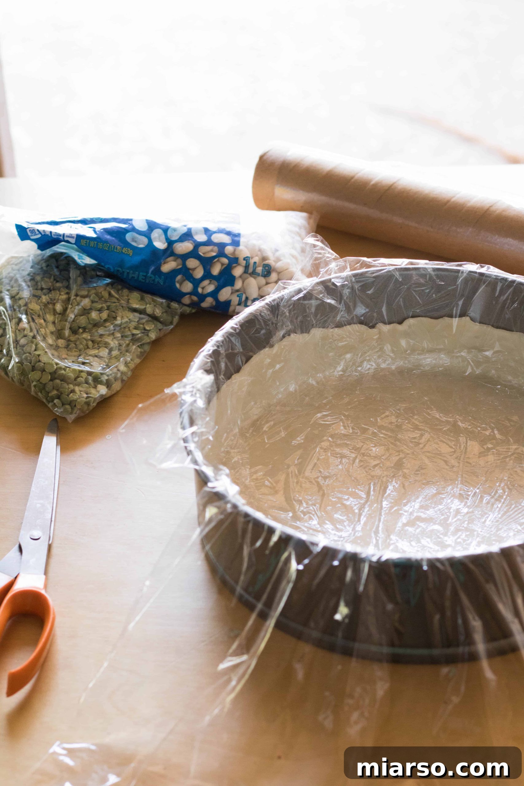 Securing dry beans with plastic wrap in a pie crust for blind baking.