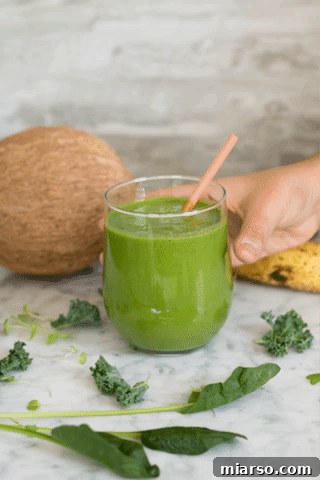 Freshly blended green smoothie in a glass with spinach and kale leaves, healthy drink