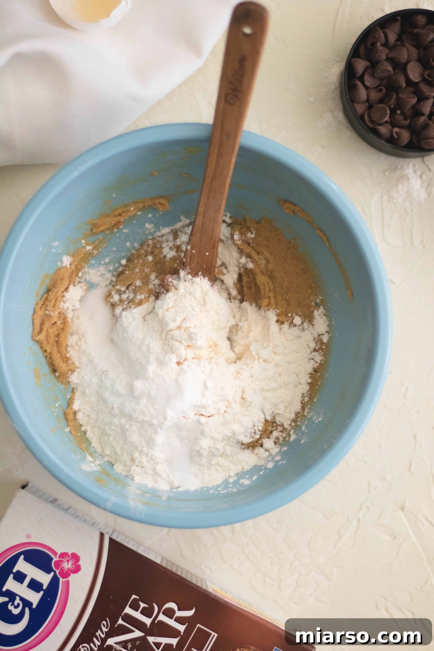 Step-by-step image showing egg yolk and vanilla extract being mixed into the cookie dough.