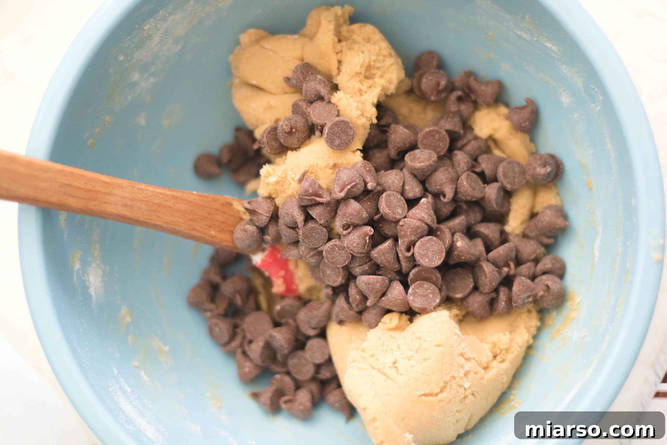 Step-by-step image of folding chocolate chips into the prepared cookie dough.