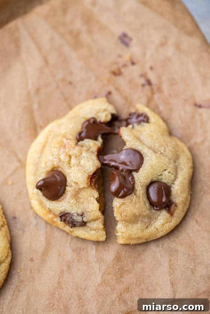 A perfectly baked chewy chocolate chip cookie, broken in half to reveal its soft, gooey center.