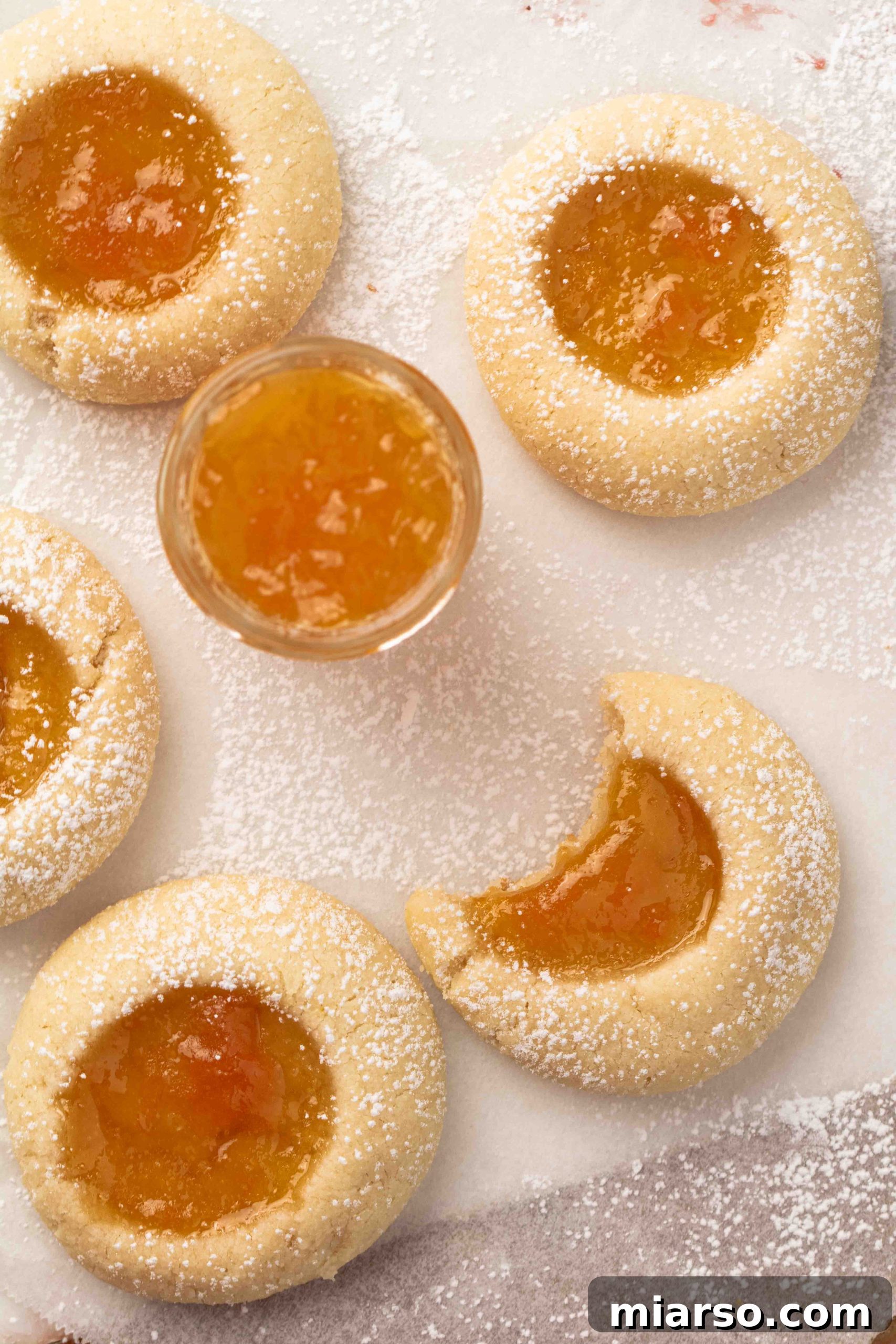 Jam-Kissed Almond Thumbprint Cookies 5 An overhead shot of vibrant apricot jam, artfully arranged next to freshly baked thumbprint cookies filled with the same sweet jam.