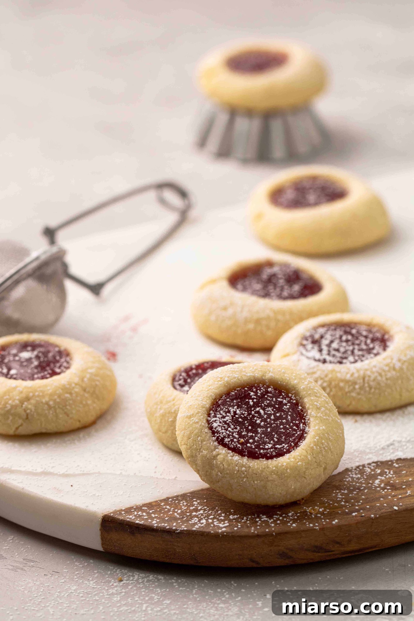 Jam-Kissed Almond Thumbprint Cookies 6 A beautifully arranged selection of homemade thumbprint cookies, some with jam and others ready for filling, on a rustic surface.
