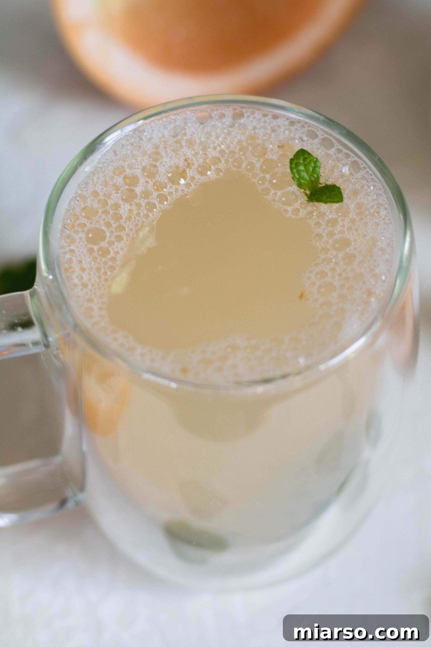 Two clear mugs of warm detox grapefruit tea, garnished, against a rustic background