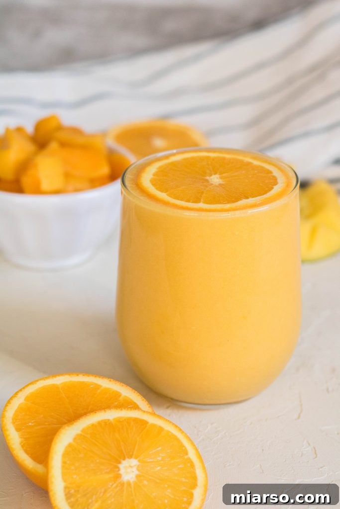 Bright orange mango smoothie in a glass with an orange slice on top, indicating an immune boost