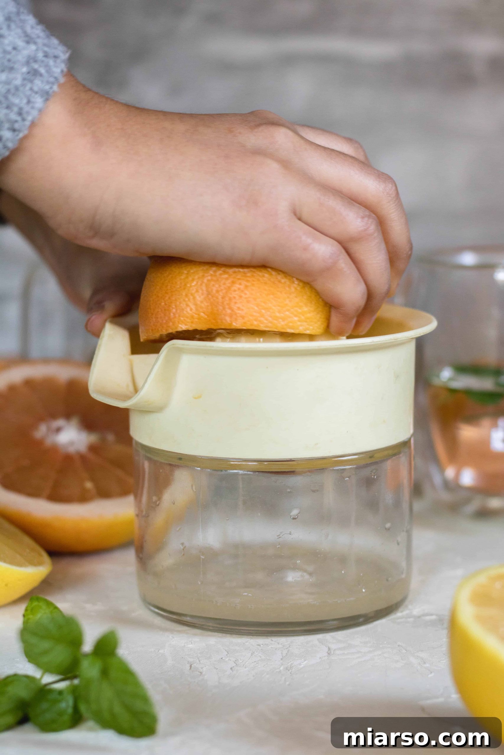 Hand squeezing fresh grapefruit juice into a bowl using a manual citrus press