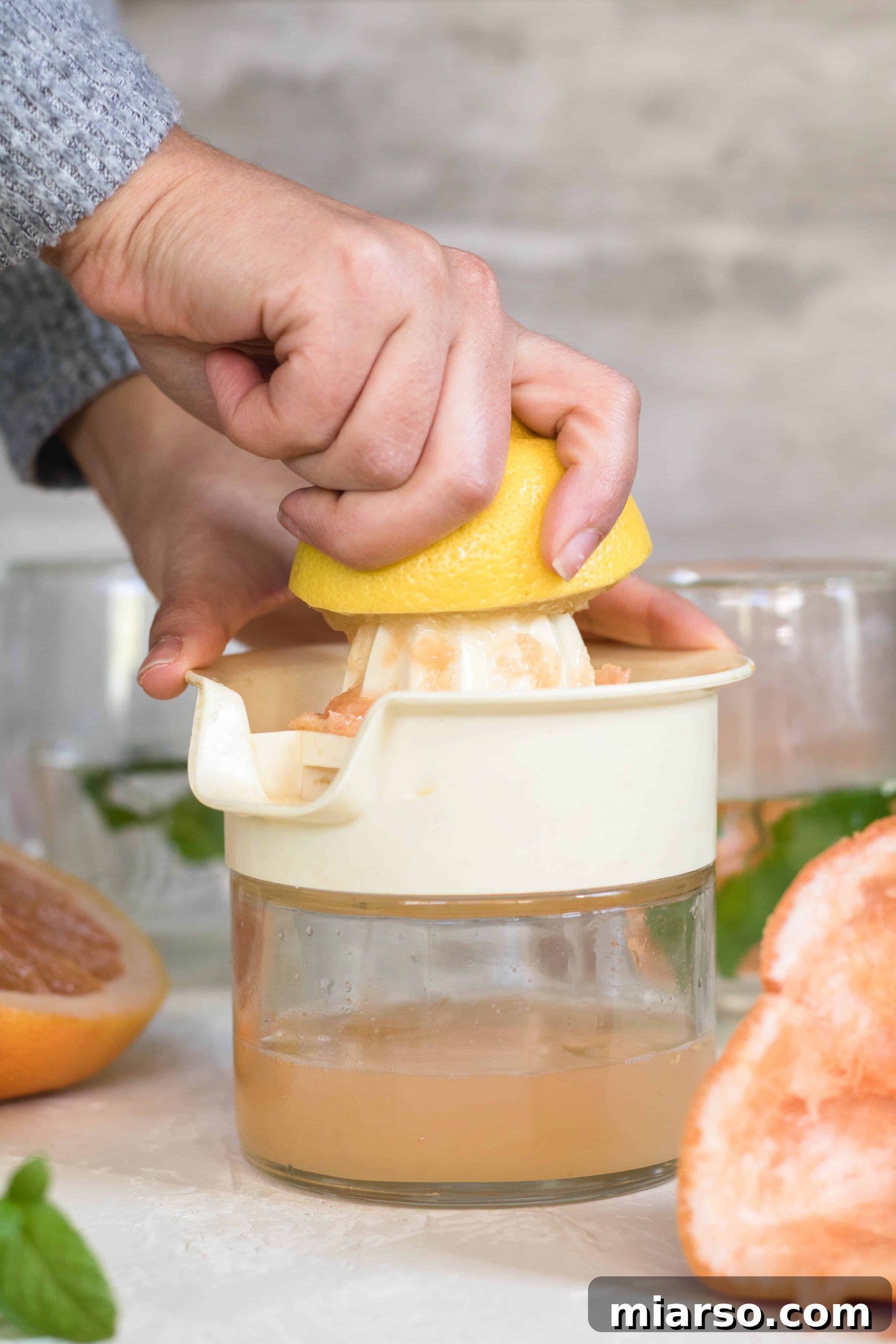 Fresh lemons being squeezed, extracting juice into a small bowl, next to grapefruit juice