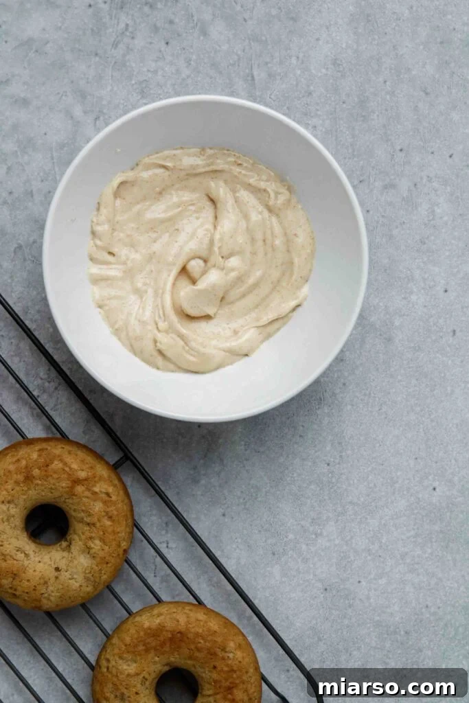 A baked banana donut being dipped into the smooth, creamy brown butter glaze, coating it evenly.