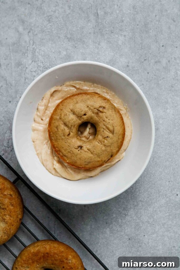 A close-up shot of a banana donut being glazed, with the excess brown butter glaze dripping off.