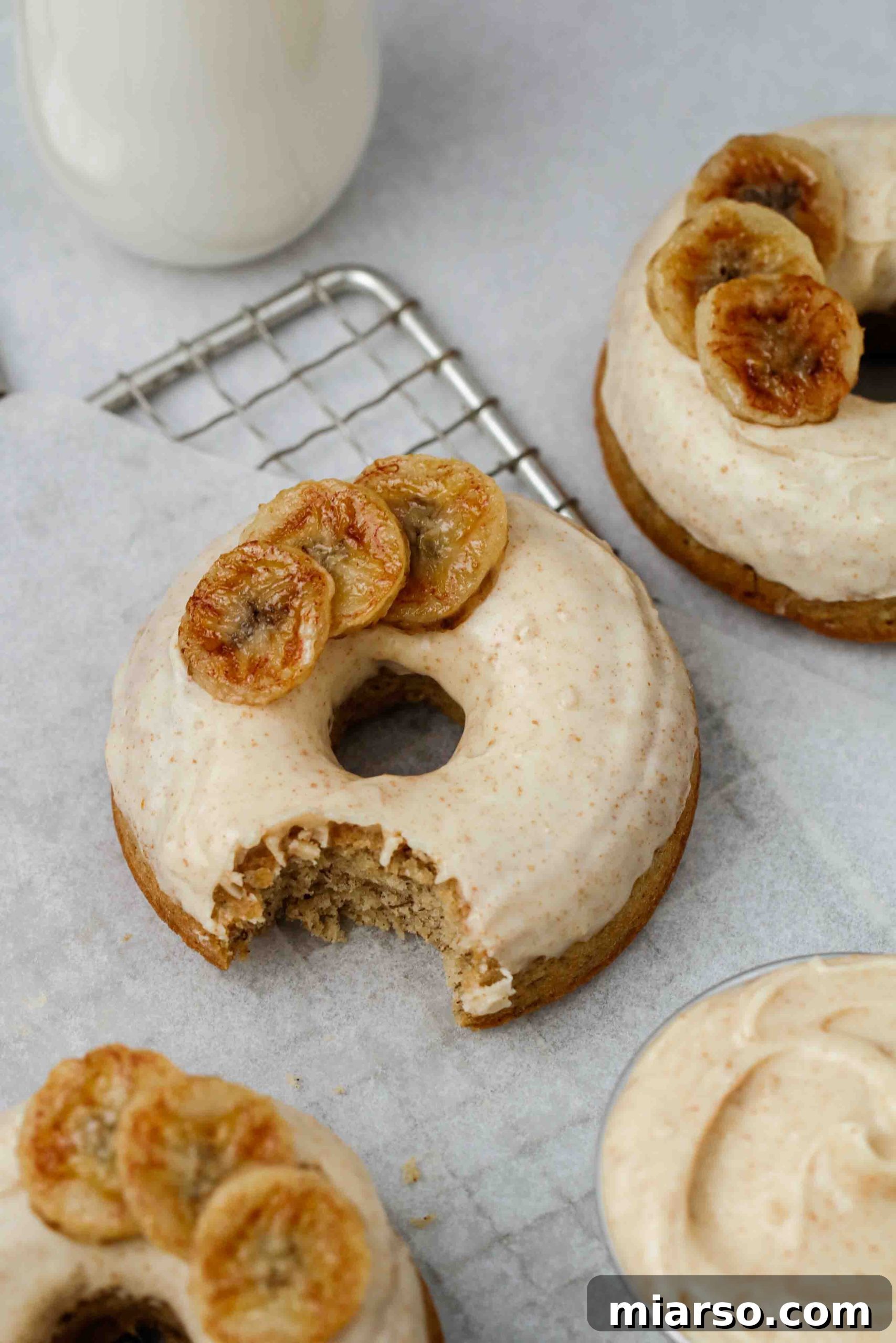 Beautifully styled photograph of a single baked banana donut with brown butter glaze on a rustic surface.