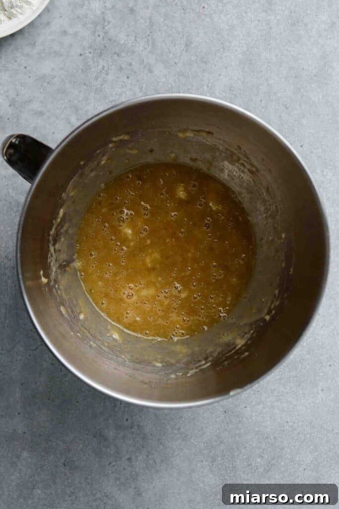 Wet ingredients for banana donuts, including mashed bananas, oil, egg, vanilla, and brown sugar, being mixed in a bowl.