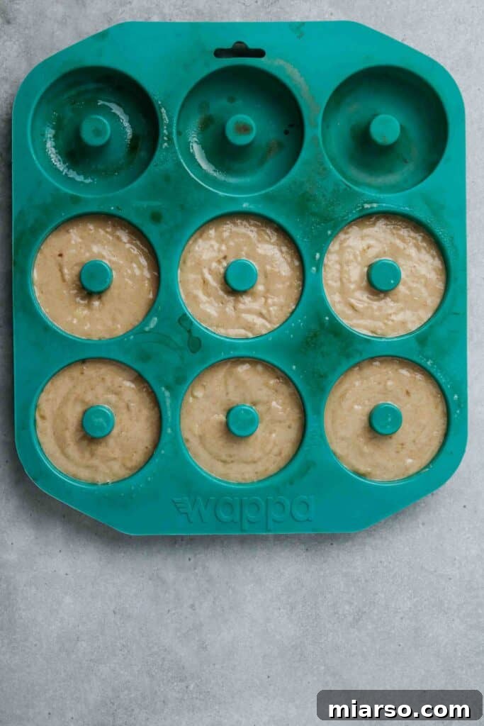 Freshly baked banana donuts, golden brown and puffed up, cooling slightly in the donut pan.